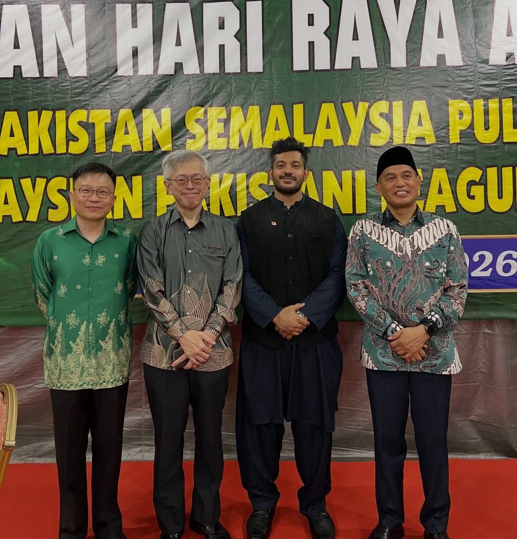 Four men posing in front of a Hari Raya banner